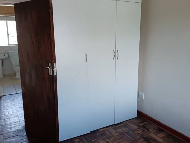 A bedroom featuring built-in cupboards and traditional parquet flooring, with a view into an adjacent bathroom.