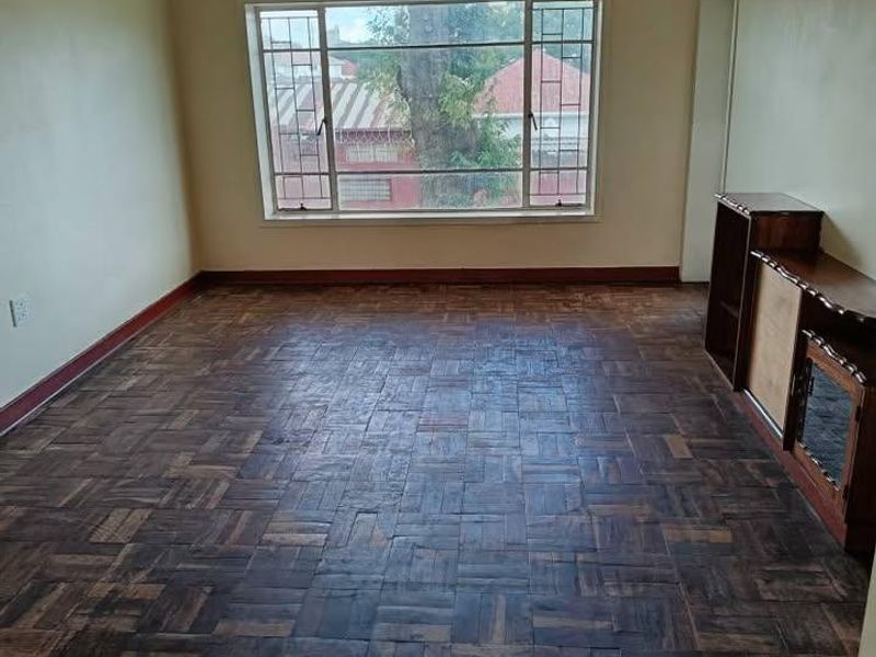 An empty living room featuring original parquet flooring, a large window providing natural light, and neutral wall finishes.