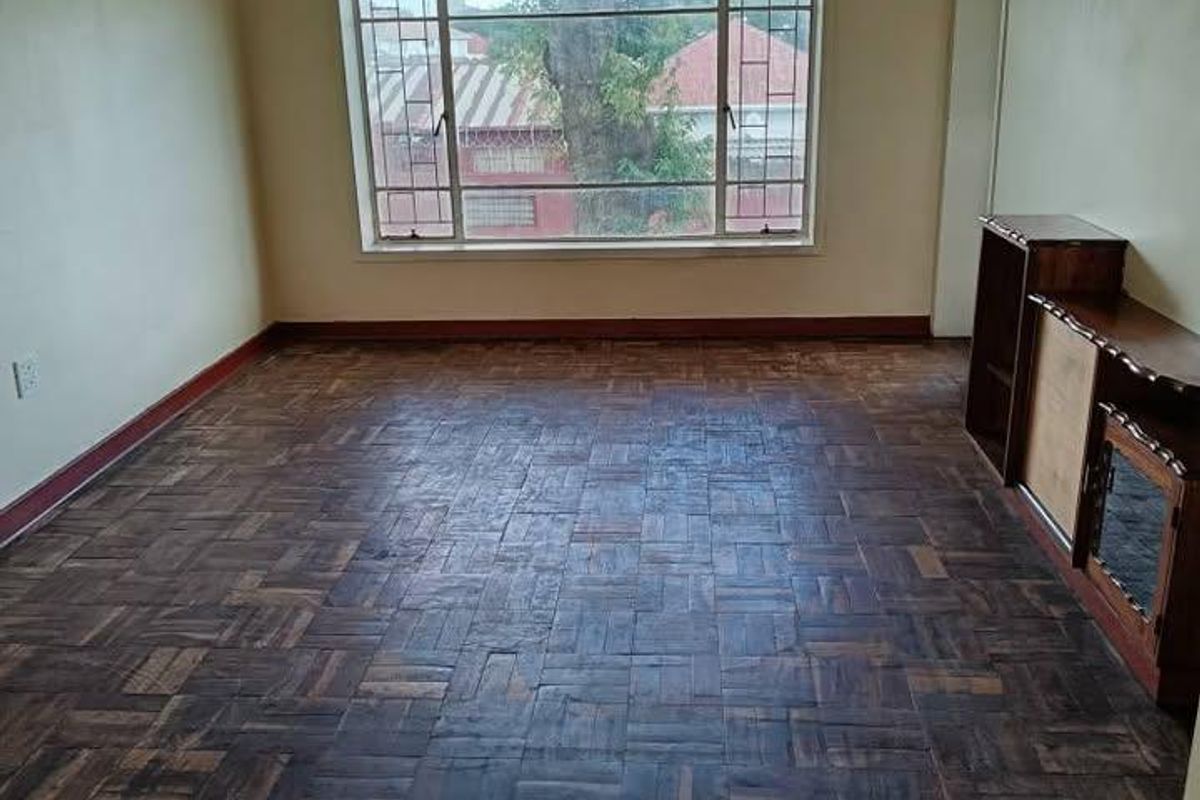An empty living room featuring original parquet flooring, a large window providing natural light, and neutral wall finishes.