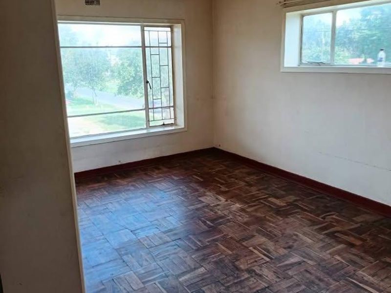 An empty living room featuring original parquet flooring, large steel-framed windows, and a neutral color palette, ready for renovation or staging.