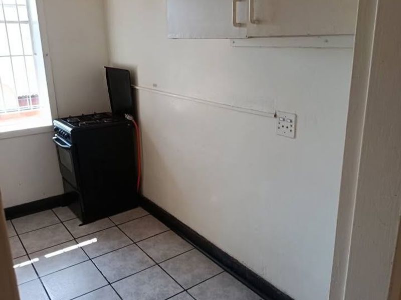 A compact kitchen area featuring tiled flooring, wall-mounted cabinetry, and a freestanding stove, requiring cosmetic updates to improve its overall condition.