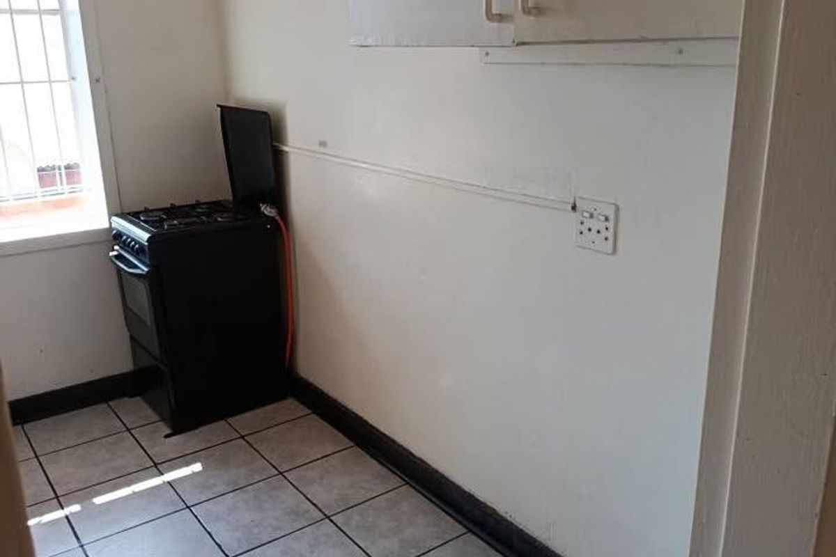 A compact kitchen area featuring tiled flooring, wall-mounted cabinetry, and a freestanding stove, requiring cosmetic updates to improve its overall condition.