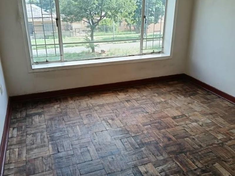 An empty bedroom featuring original parquet flooring and a large window providing natural light and street views.