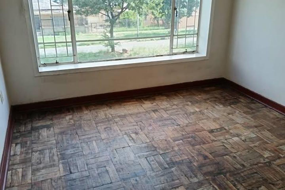 An empty bedroom featuring original parquet flooring and a large window providing natural light and street views.