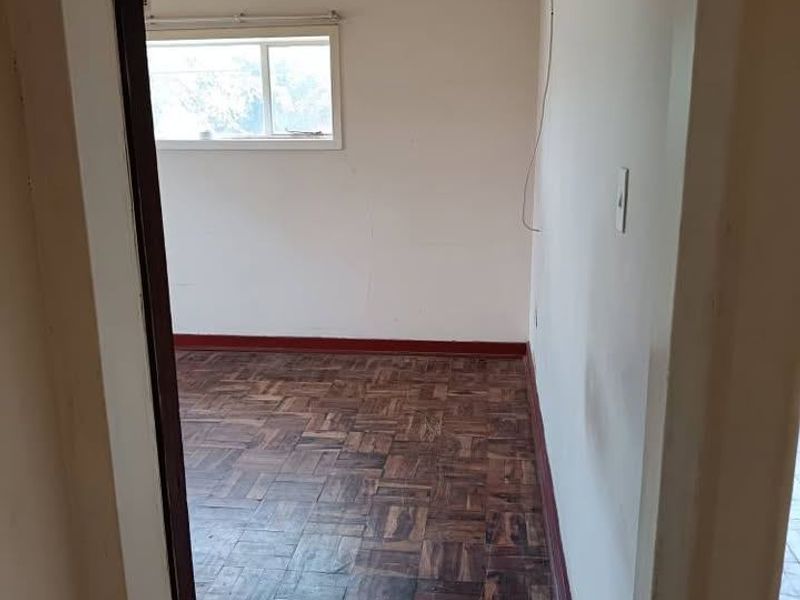 An empty bedroom featuring original parquet flooring, a sliding window, and visible wall imperfections, offering a blank canvas for renovation.