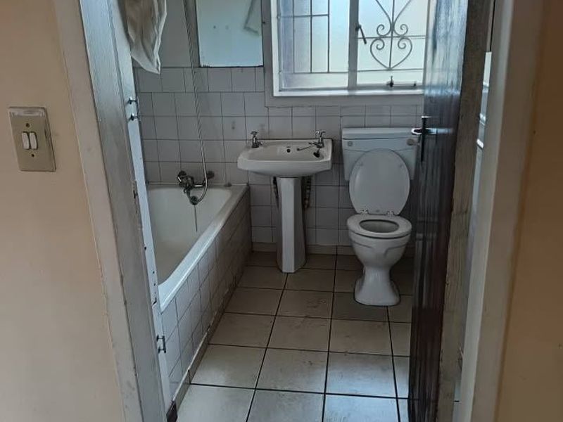 A dated bathroom featuring a pedestal basin, standard toilet, and a bathtub with shower mixer, finished with ceramic wall and floor tiles.