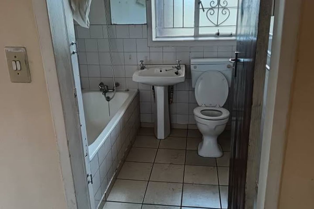 A dated bathroom featuring a pedestal basin, standard toilet, and a bathtub with shower mixer, finished with ceramic wall and floor tiles.