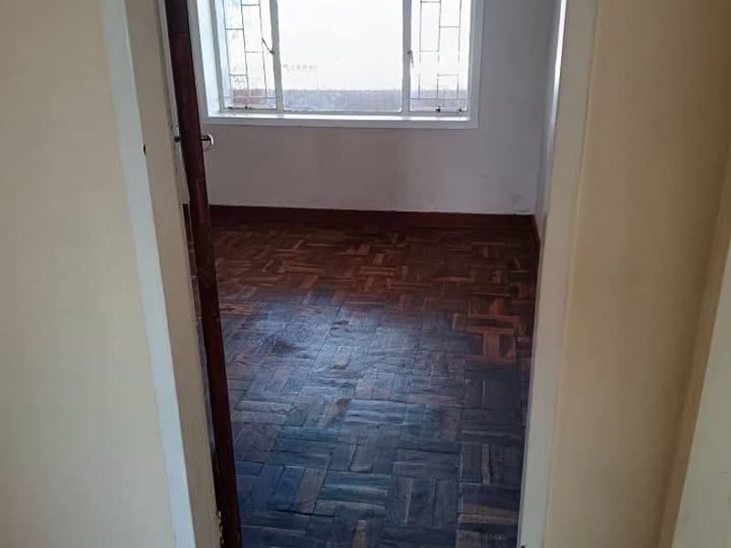 An empty bedroom featuring original parquet flooring and a window with security bars, offering a blank canvas for renovation and interior design.