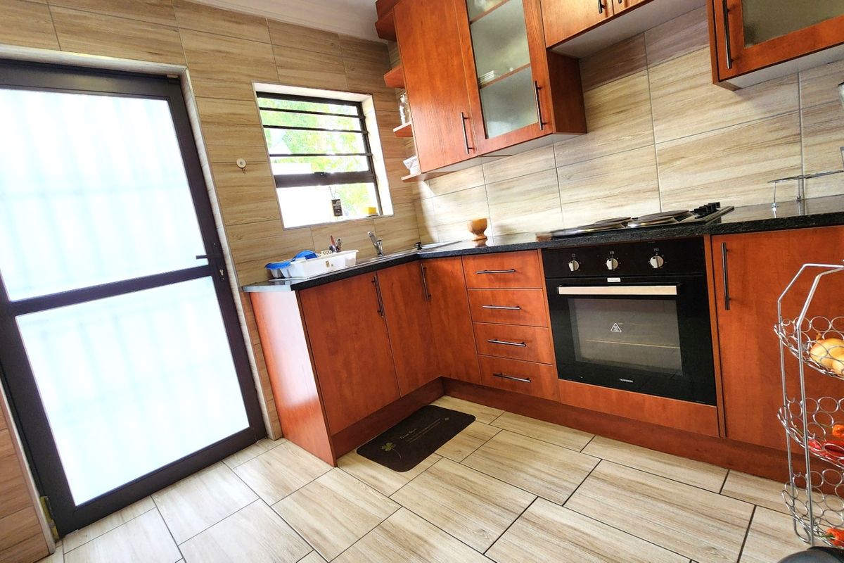 A functional kitchen featuring warm-toned wooden cabinetry, granite countertops, a built-in oven, gas hob, and modern tiled finishes throughout.