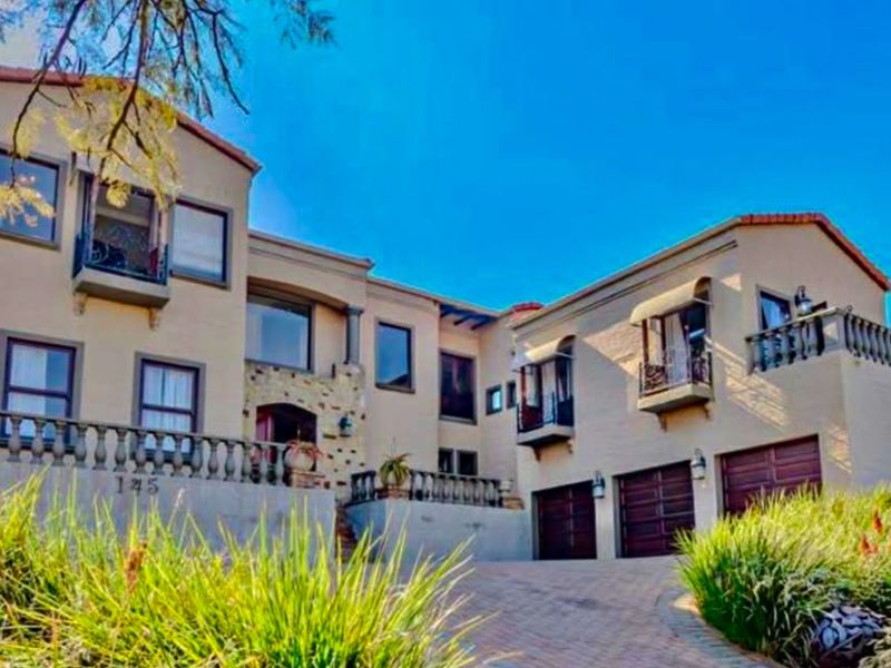 A large multi-level residential property featuring a triple garage, stone facade accents, and upper-level balconies with classic balustrades.