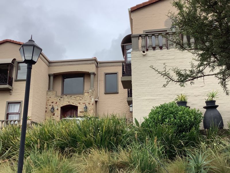 Front elevation of a multi-story house featuring stone cladding, painted brickwork, and an upper-level balcony with a classic balustrade.