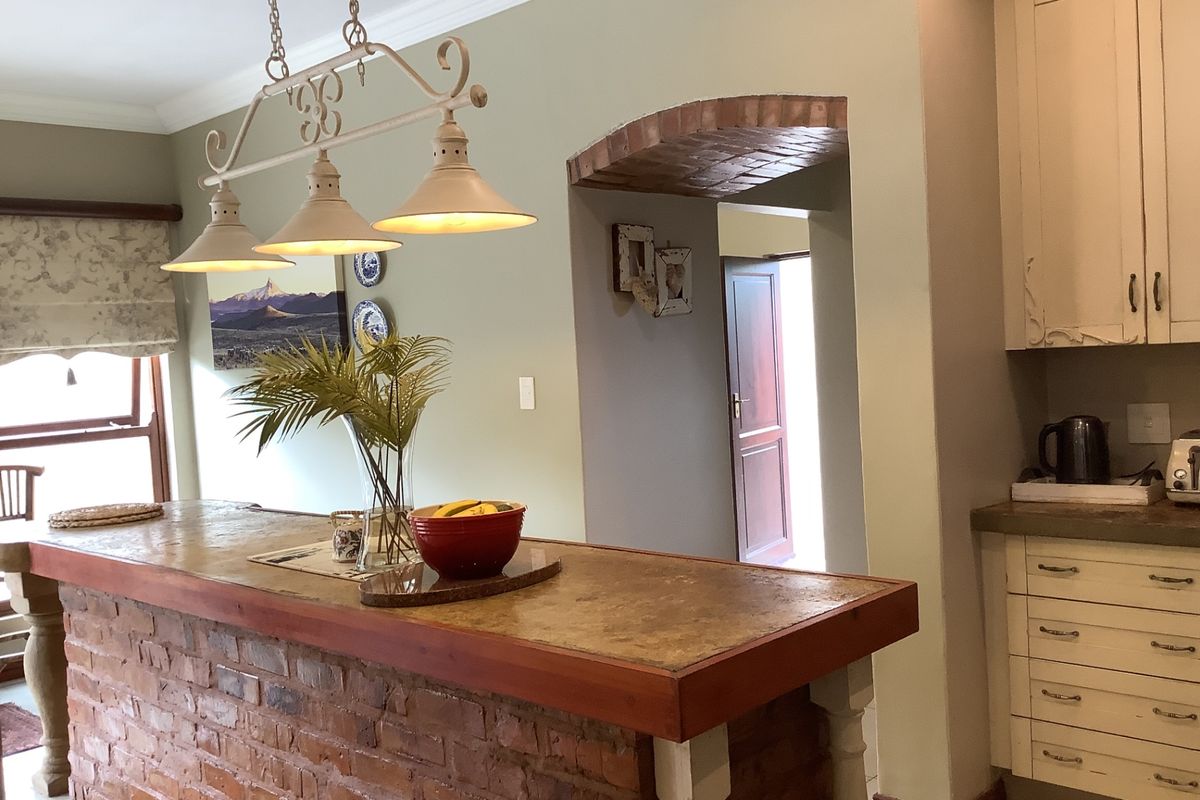 A rustic kitchen featuring a brick-based island with a stone countertop, complemented by an arched doorway and traditional cabinetry.