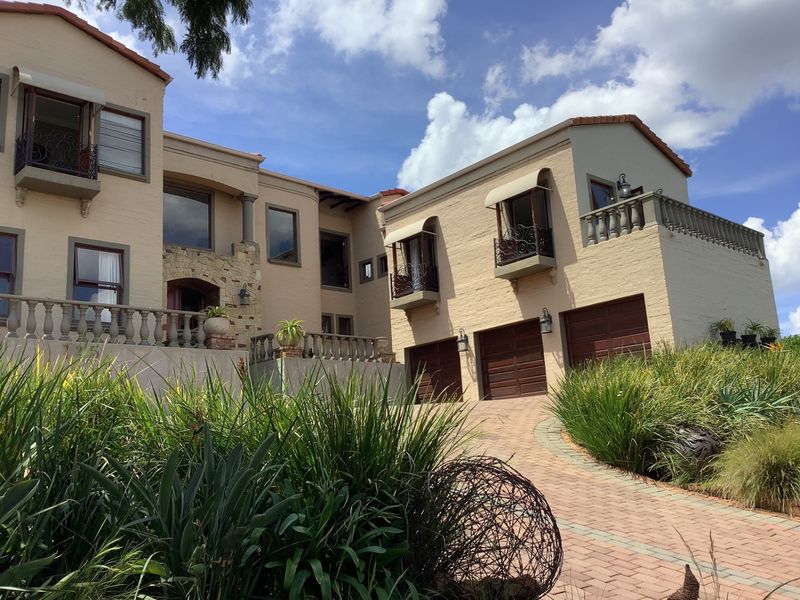 A substantial multi-level residence featuring a triple garage, stone-clad entrance, and decorative balustrades, set against a landscaped driveway and clear blue sky.