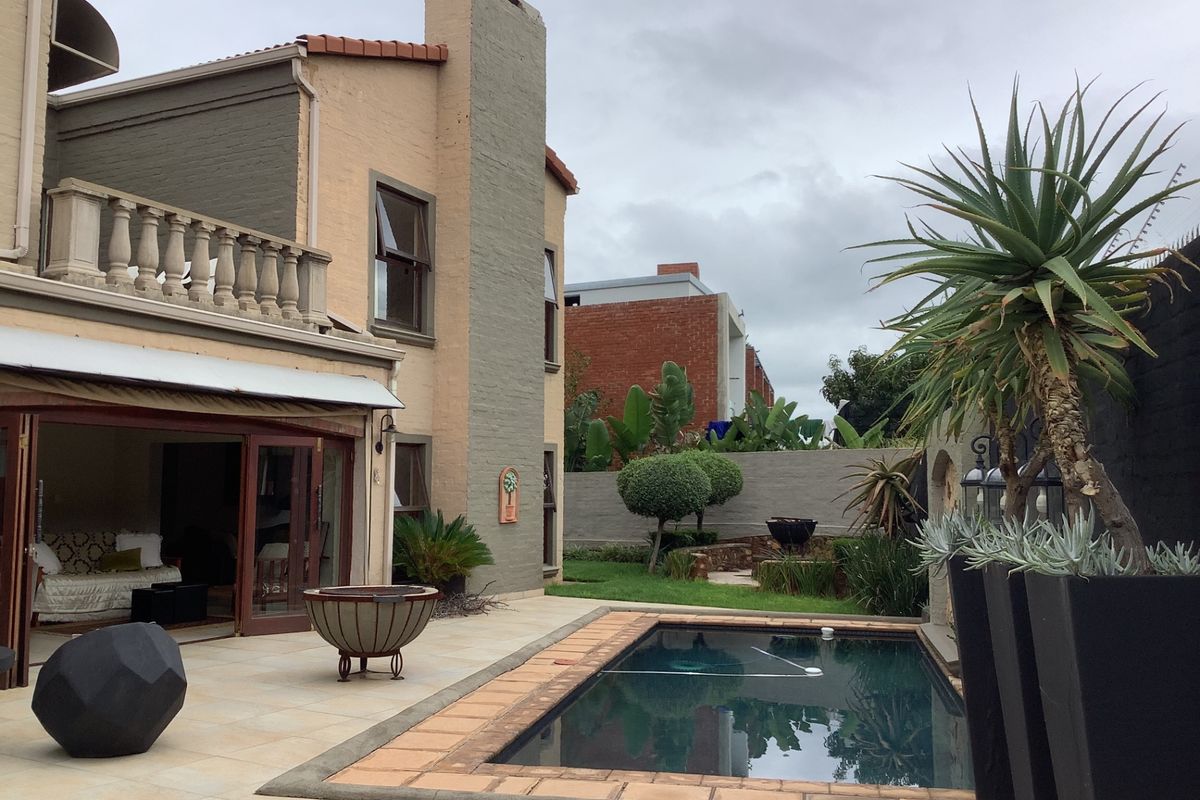 Rear exterior view featuring a swimming pool, paved patio area, and a multi-story building facade with a balcony and sliding door access.