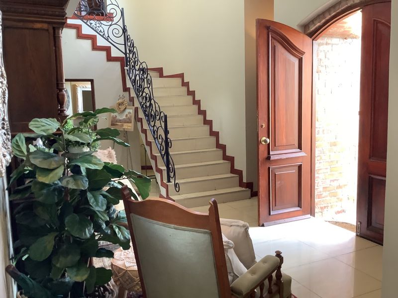 Welcoming entrance foyer featuring a classic staircase with decorative wrought iron railings, tiled flooring, and a solid timber front door opening to brickwork.