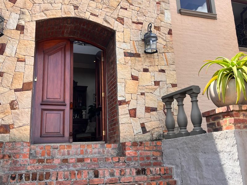 Front entrance featuring a solid timber door, stone-clad facade, and brick steps with decorative balustrades.