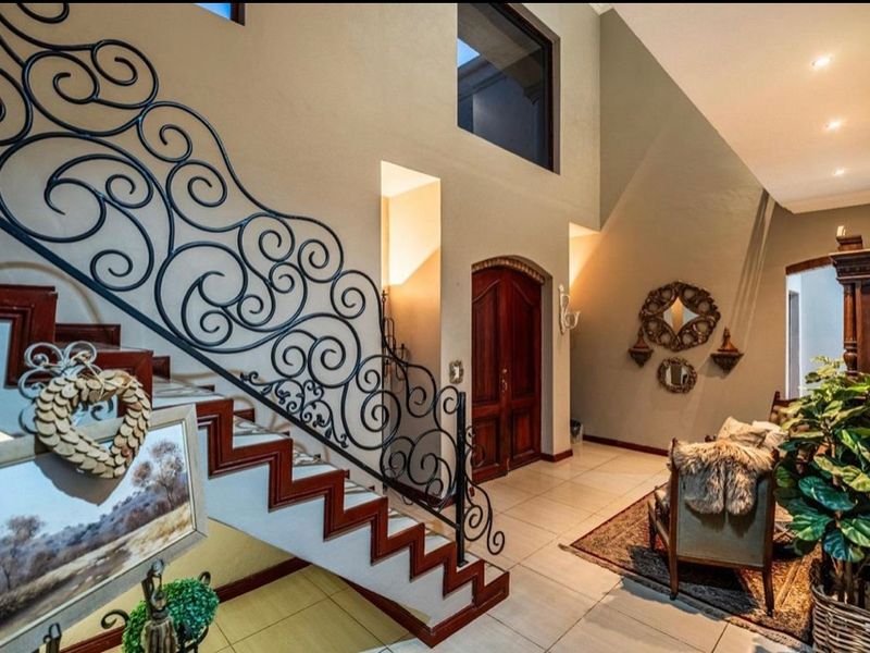 Spacious double-volume entrance hall featuring a grand wooden staircase with ornate wrought iron balustrades and elegant double front doors.