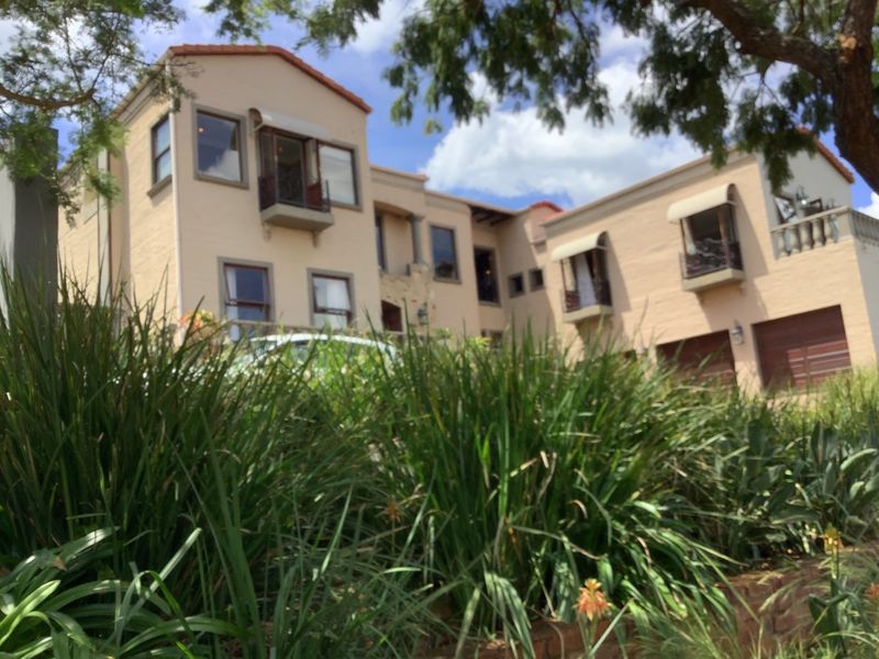 Front elevation of a multi-story residential property featuring a double garage, balconies with awnings, and a tiled roof structure.