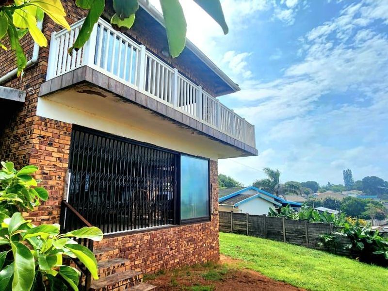 Rear view of a double-story face brick house featuring an upper-level balcony with white balustrades and a lower-level sliding door with security gate.