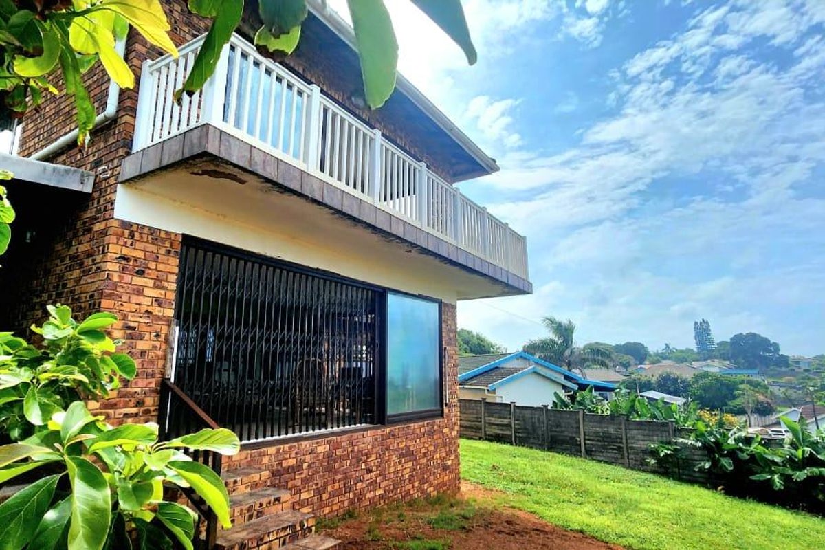 Rear view of a double-story face brick house featuring an upper-level balcony with white balustrades and a lower-level sliding door with security gate.