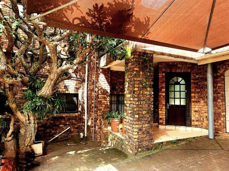 Front exterior view featuring a face brick facade, covered entrance, paved driveway, and a shade sail structure over the garage area.