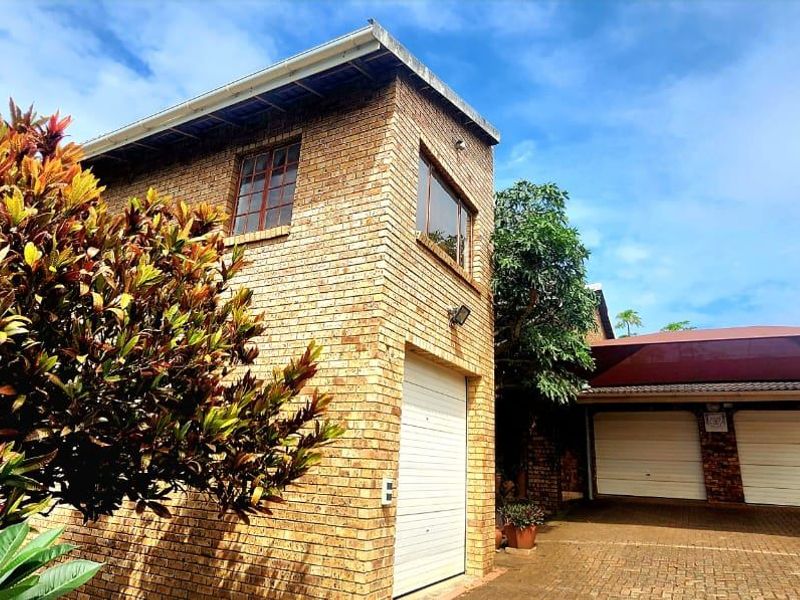 Front exterior view of the property featuring face brick construction, a double garage with shade cloth carport, and a paved driveway.