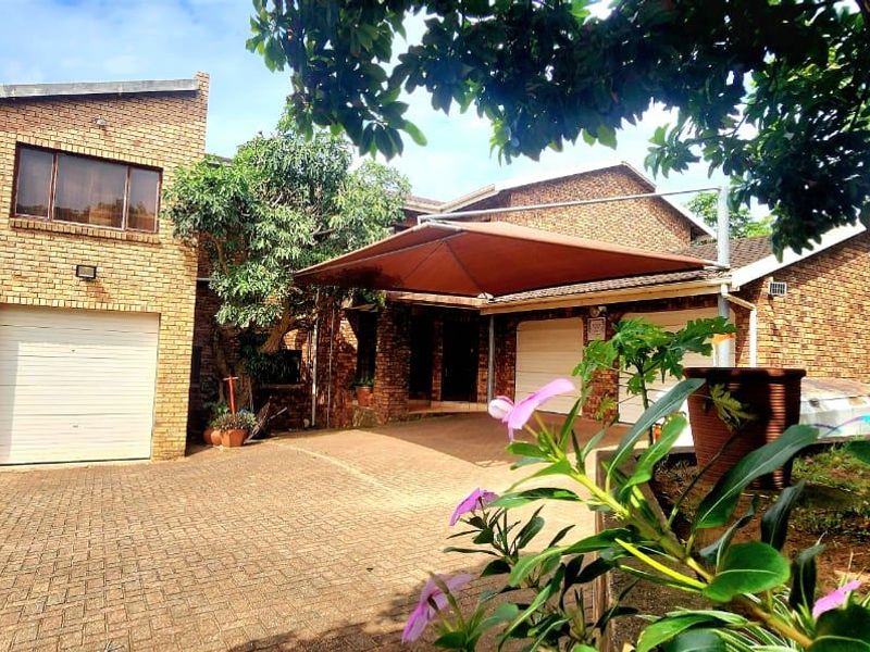 Front view of a double-story face brick house featuring a paved driveway, double garage, and a shade sail over the entrance area.
