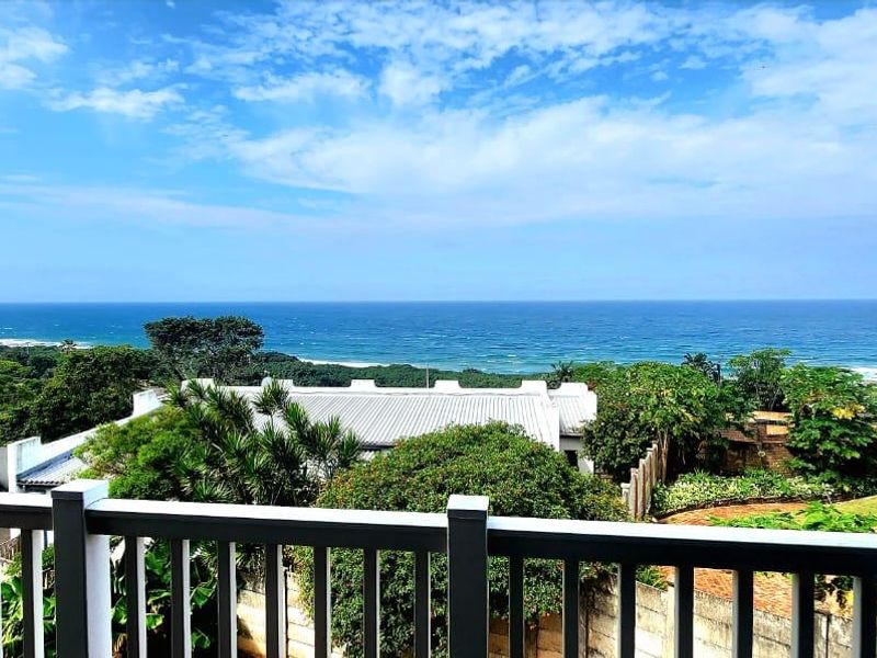 Elevated coastal view overlooking the ocean, surrounding greenery, and residential neighborhood from a balcony.