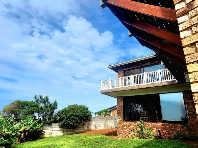 Rear view of a multi-story face brick house featuring a balcony with white railings, timber roof beams, and a private garden area.