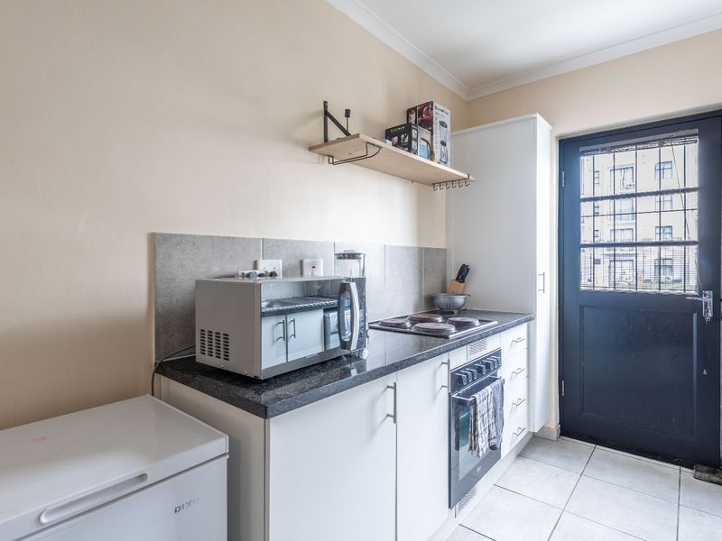 A functional kitchen featuring granite countertops, built-in oven, electric hob, tiled backsplash, and direct access to the exterior via a secure door.