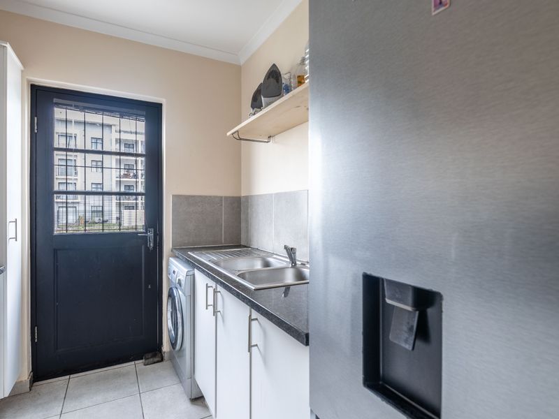 Functional scullery area featuring built-in cabinetry, granite countertops, a double sink, and direct access to the exterior via a security door.