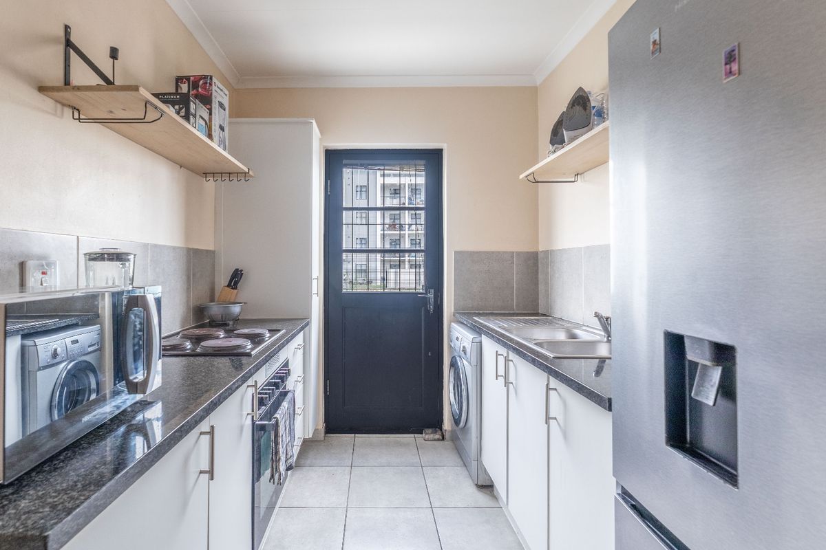 Functional galley-style kitchen featuring granite countertops, built-in oven and hob, tiled backsplash, and direct access to the exterior via a secure door.
