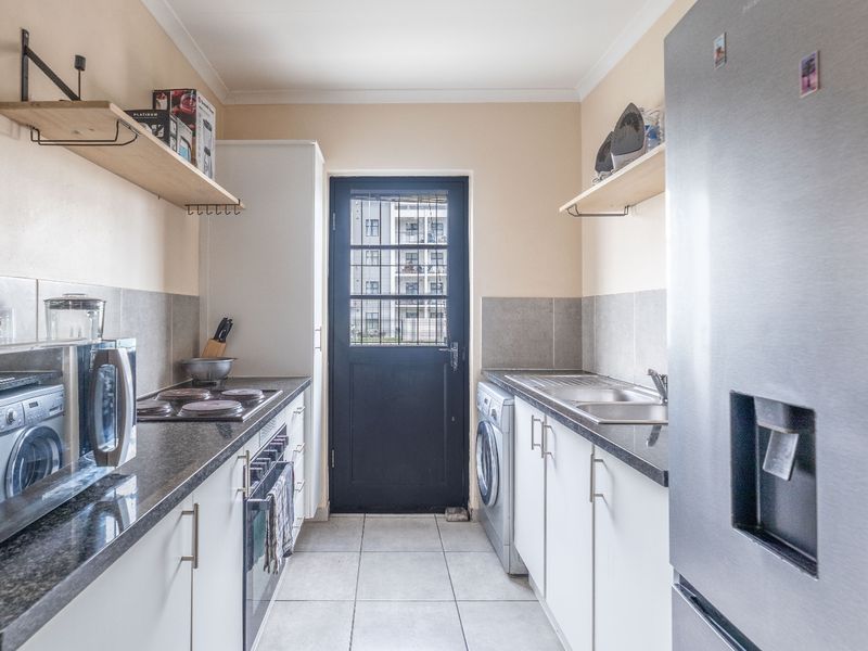 Functional galley-style kitchen featuring granite countertops, built-in oven and hob, tiled backsplash, and direct access to the exterior via a secure door.