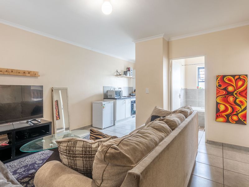 Open-plan living area featuring tiled flooring and a compact kitchen space, with direct access to an adjacent bathroom.