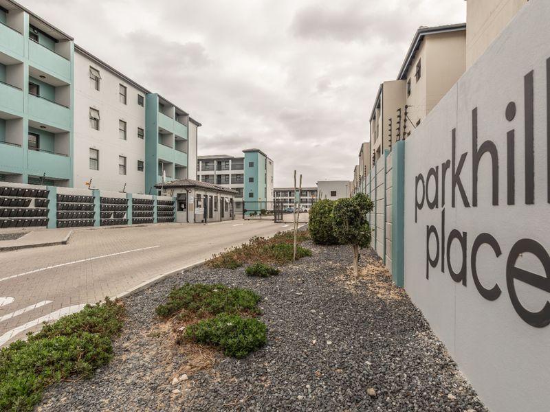 Street view of the Parkhill Place apartment complex entrance, featuring a secure gated access point, paved driveway, and modern building facade.