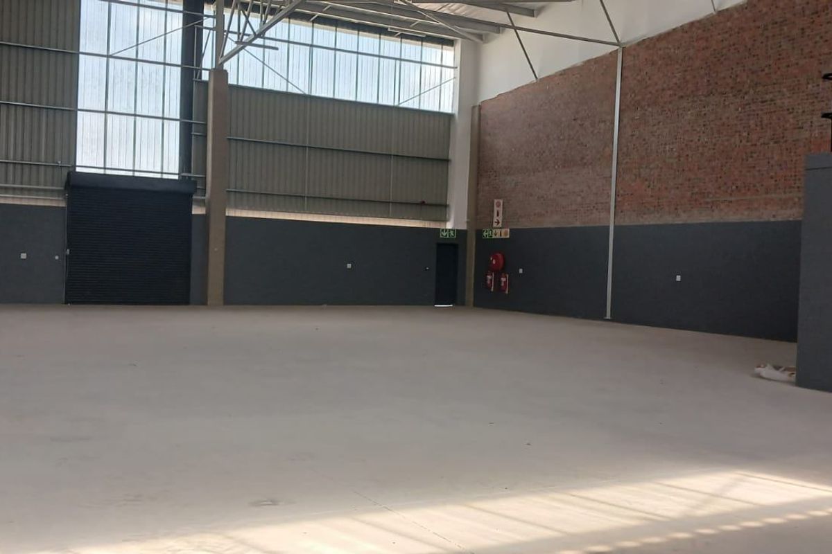 Spacious industrial warehouse unit featuring high ceilings, concrete flooring, a roller shutter door, and a mezzanine level, suitable for various commercial or storage operations.