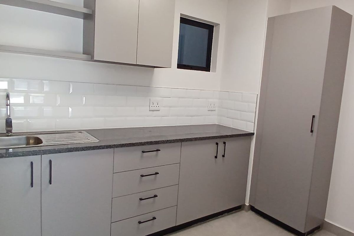 A modern, clean kitchen area featuring grey cabinetry, a stainless steel sink, subway tile backsplash, and a tall pantry cupboard.
