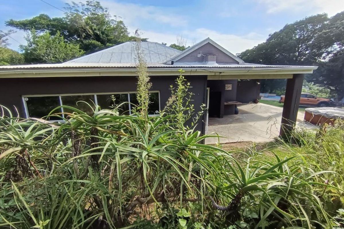 Rear view of the property featuring a covered patio area with a built-in braai and a corrugated metal roof.