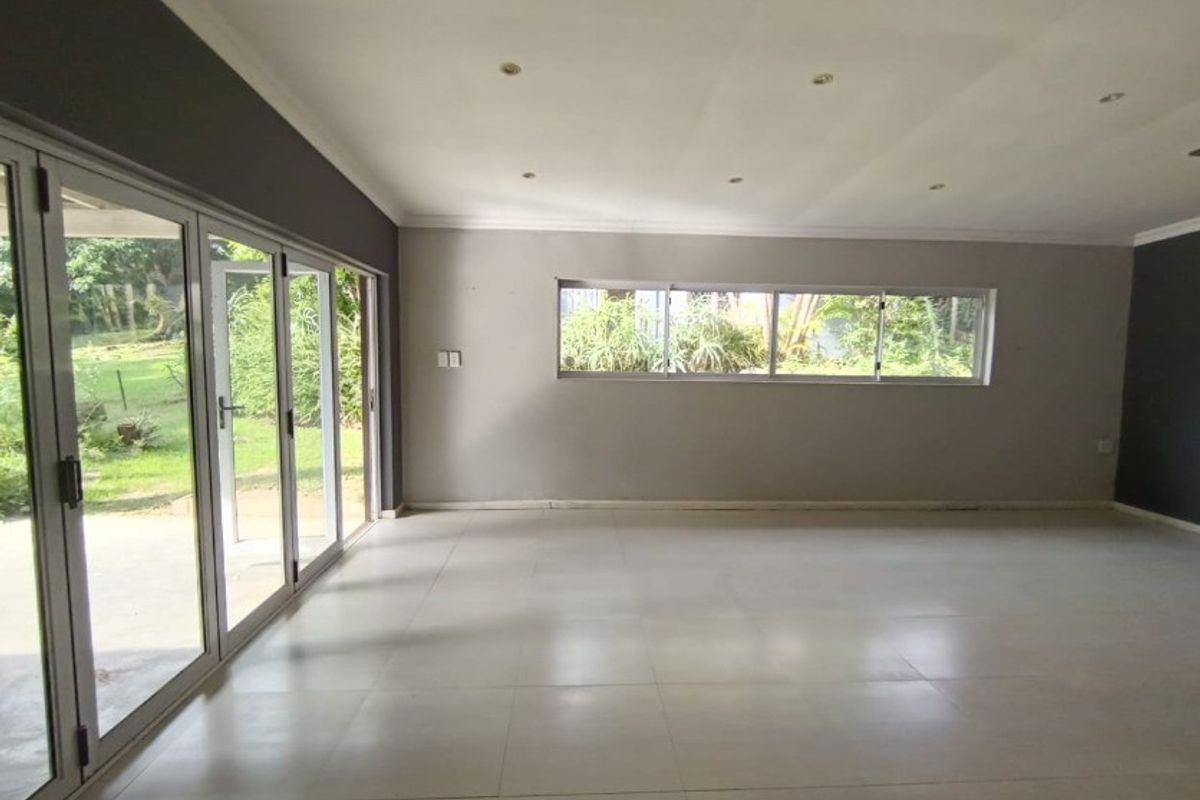 Spacious, empty living area featuring neutral tiled floors, recessed lighting, and large aluminium sliding doors providing direct access to the garden.