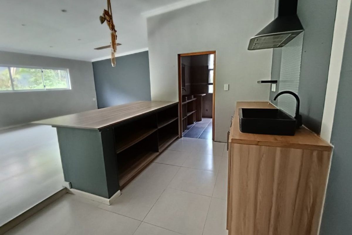 Modern kitchen area featuring a central island, sleek cabinetry, black sink fixtures, and an extractor fan, leading into an adjacent scullery space.