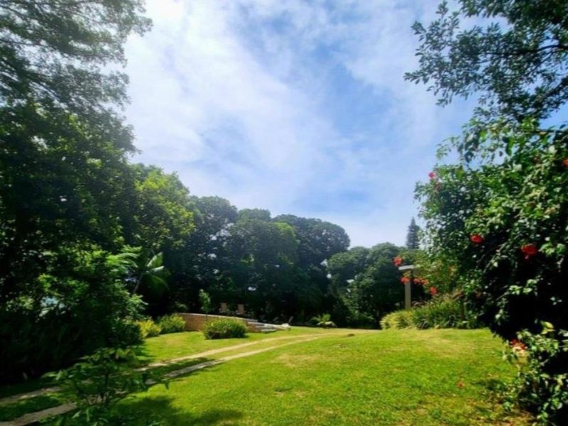 A spacious, well-maintained garden featuring mature trees, lush green lawn, and a stone pathway leading through the property grounds.
