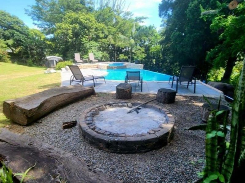 Outdoor entertainment area featuring a swimming pool with a paved deck and a stone fire pit set within a landscaped garden.