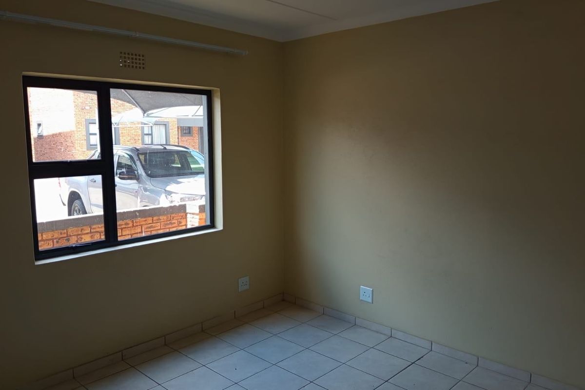 An empty bedroom featuring tiled flooring, neutral wall paint, and an aluminium-framed window providing natural light.