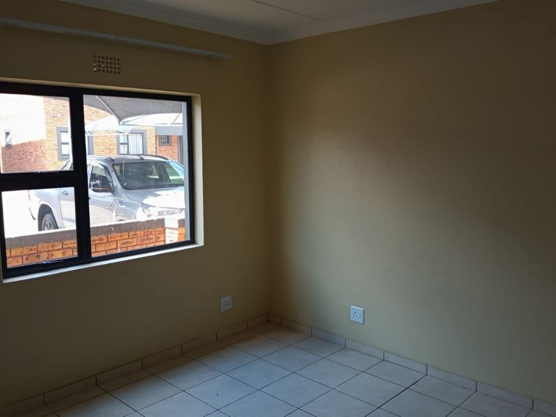 An empty bedroom featuring tiled flooring, neutral wall paint, and an aluminium-framed window providing natural light.