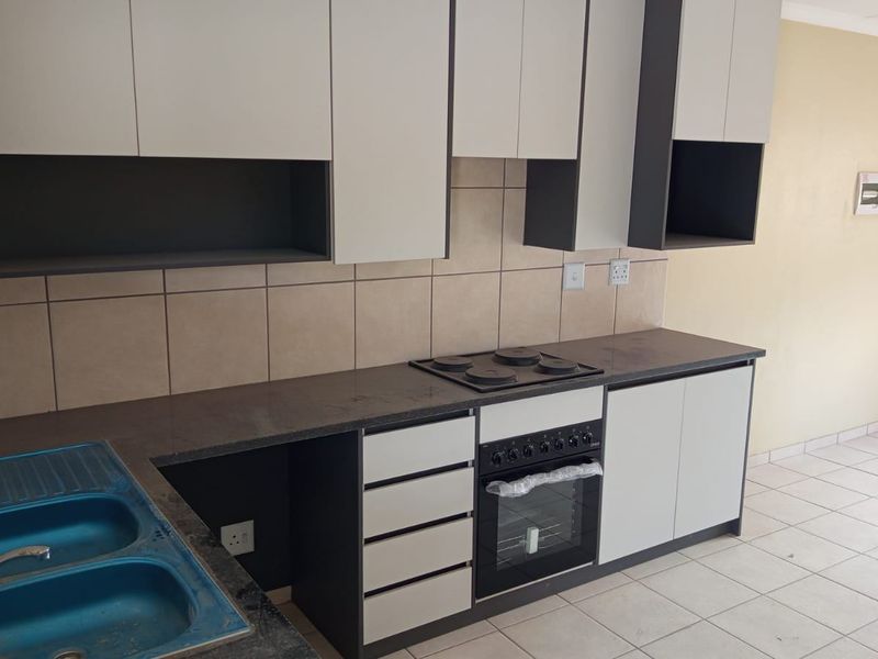 A modern, clean kitchen featuring two-tone cabinetry, stone countertops, a built-in oven and hob, and tiled flooring in an open-plan layout.