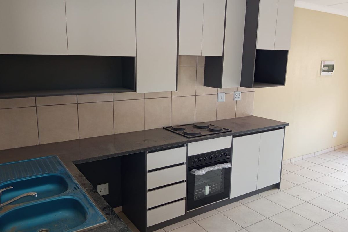 A modern, clean kitchen featuring two-tone cabinetry, stone countertops, a built-in oven and hob, and tiled flooring in an open-plan layout.
