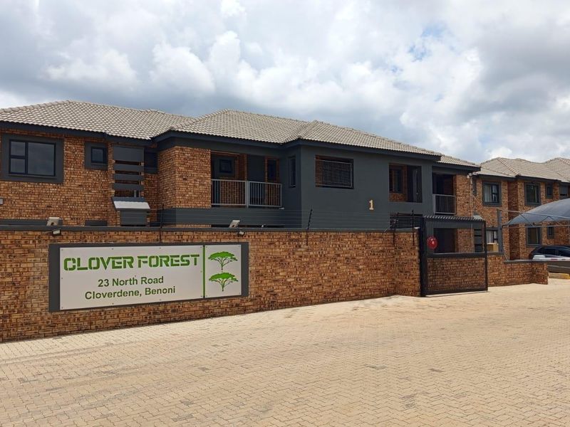 Front exterior view of Clover Forest apartment complex featuring face brick architecture, paved driveway, and secure gated access.