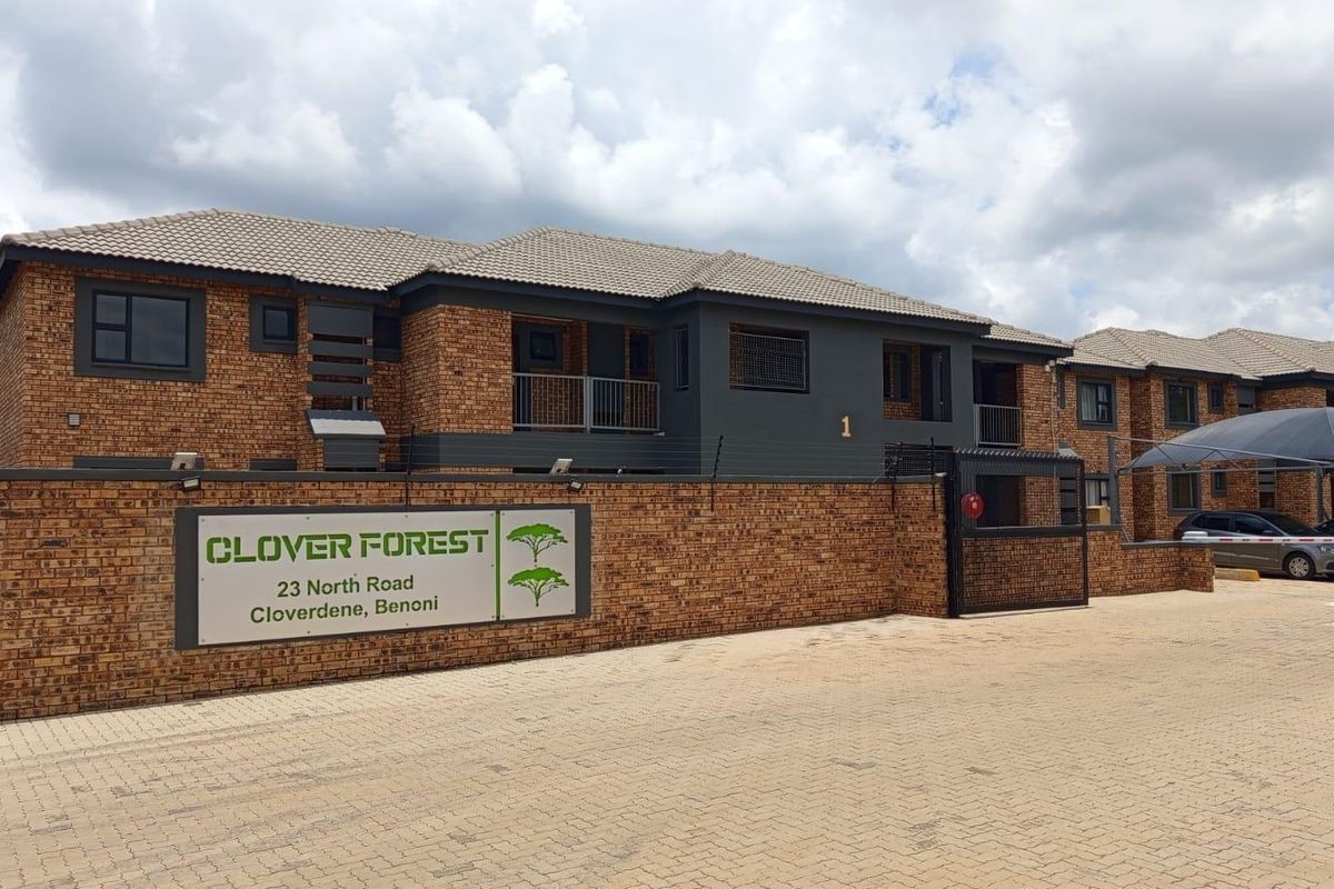 Front exterior view of Clover Forest apartment complex featuring face brick architecture, paved driveway, and secure gated access.