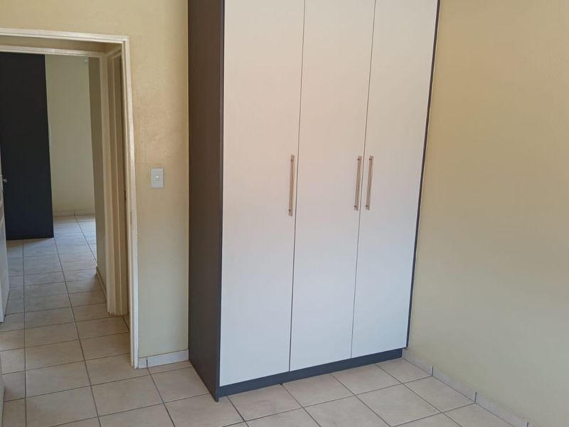 A clean, empty bedroom featuring neutral tiled flooring and a modern, white built-in wardrobe with dark trim.