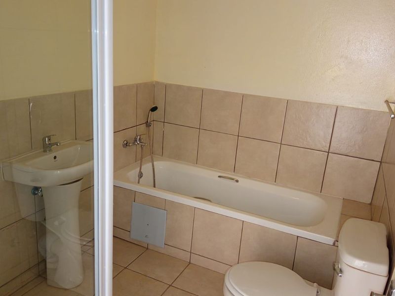 A functional bathroom featuring a pedestal basin, bathtub with handheld shower, and a separate shower enclosure with neutral wall and floor tiling.